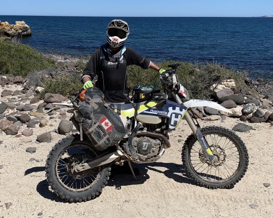 Peter Stace-Smith, on a fully-loaded adventure motorcycle beside a stream.